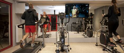 Un gimnasio con cintas de correr, elípticas y una pantalla de televisión.