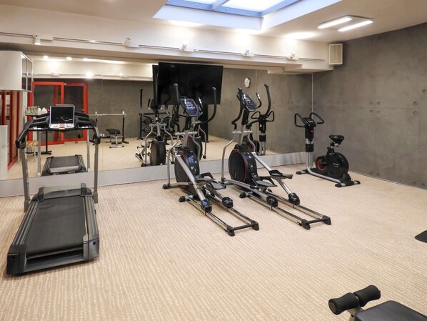 A gym with treadmills, elliptical machines, and a mirror wall.