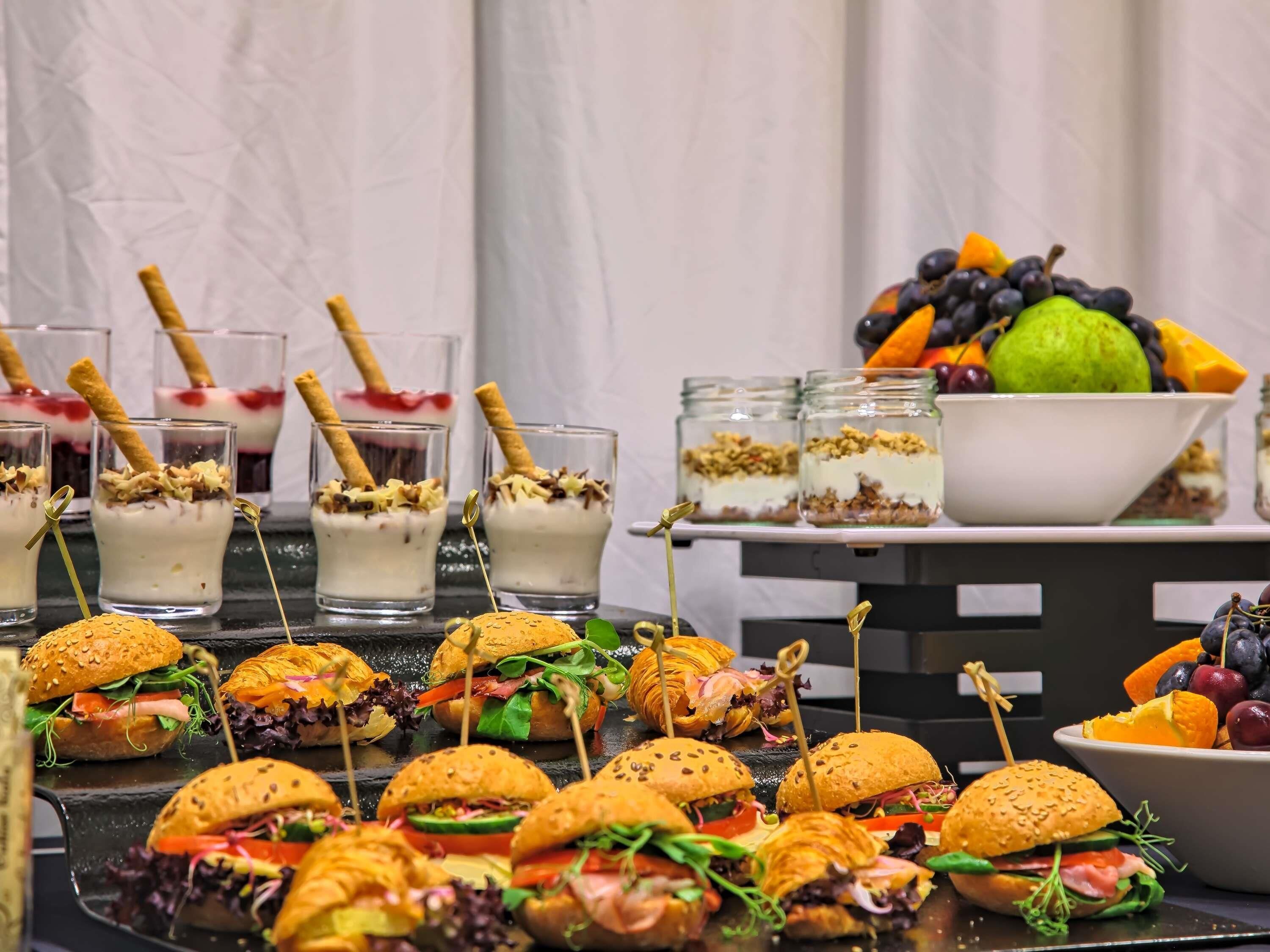A buffet table with mini sandwiches, fruit bowls, and layered desserts.
