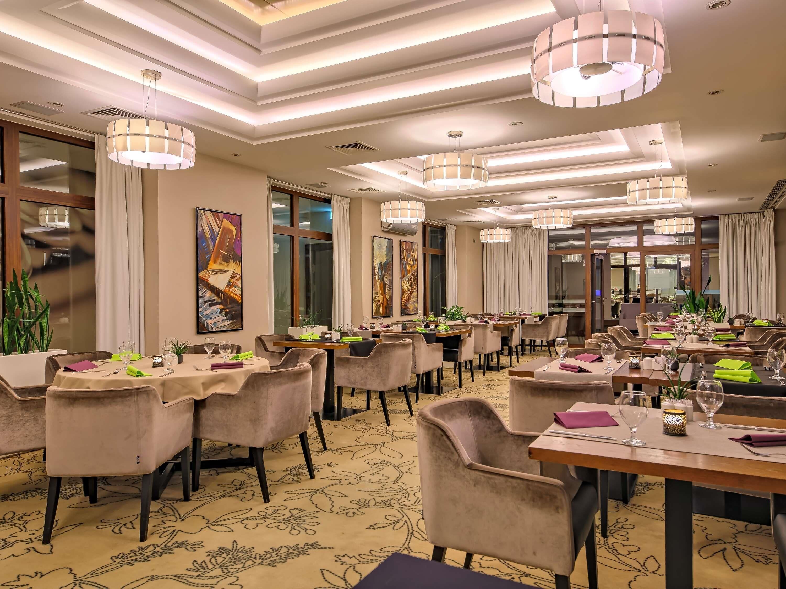 Un espace de restauration d’hôtel comprenant plusieurs tables, des chaises et des luminaires suspendus.