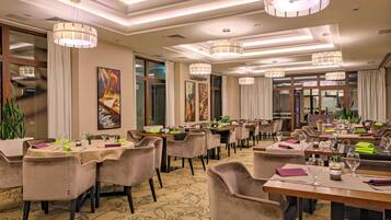 Comedor de hotel con varias mesas, sillas y lámparas colgantes.