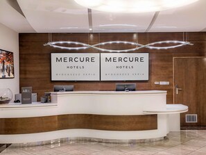 Un comptoir d’accueil d’hôtel avec deux grands panneaux indiquant « Hôtels Mercure », un écran numérique et un luminaire moderne.