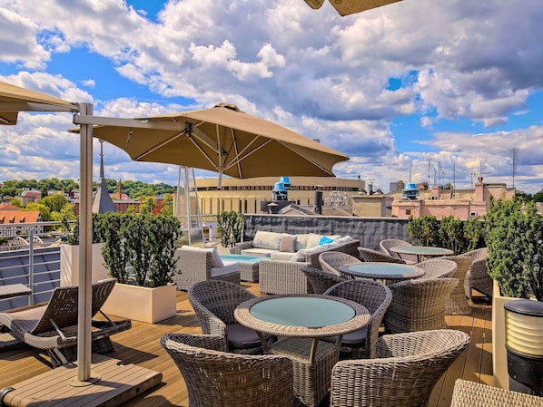 A rooftop terrace with wicker furniture, a pool table, and a large umbrella.