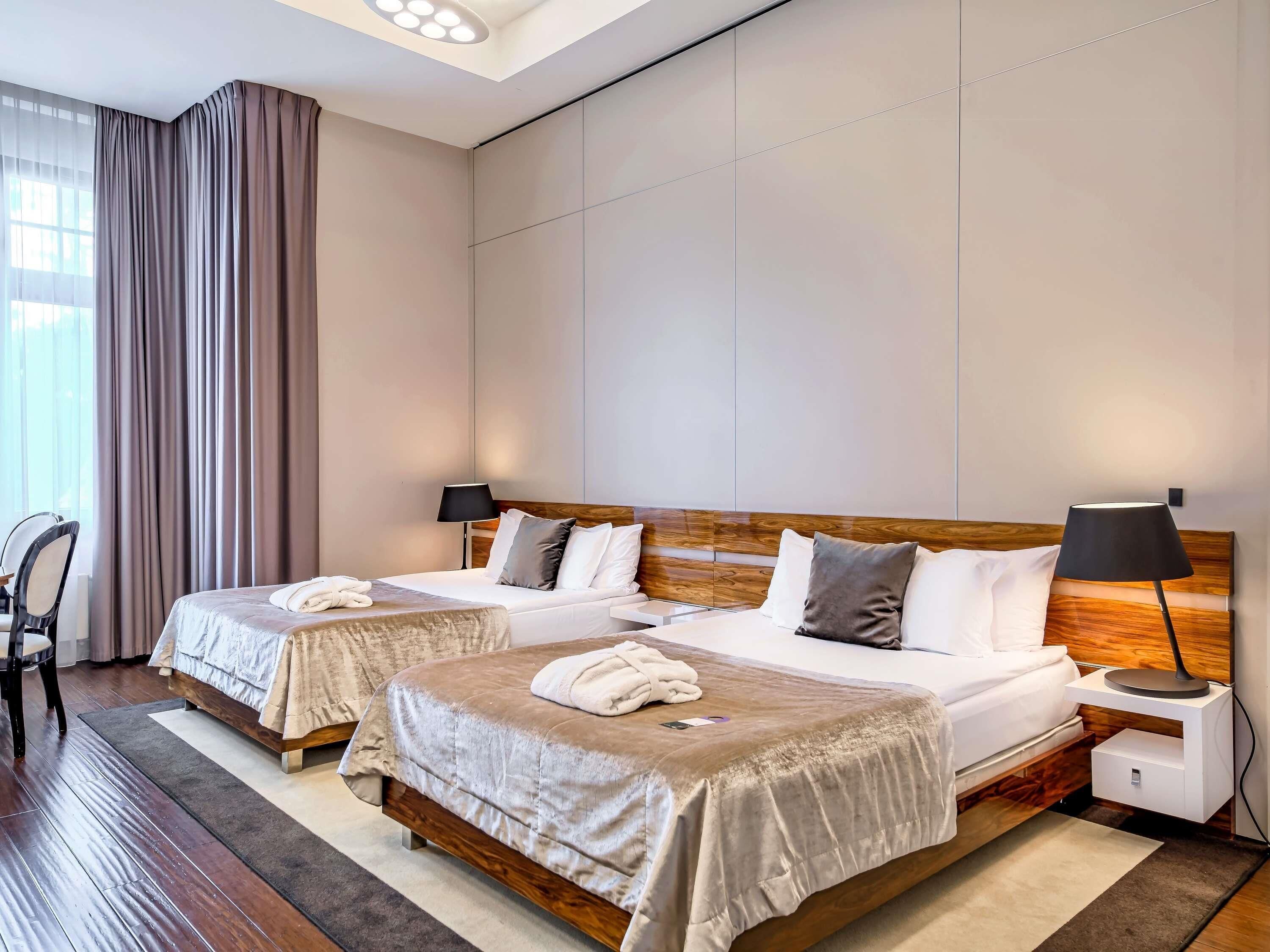 Una habitación de hotel con dos camas, un escritorio, una silla y un ventanal con cortinas.