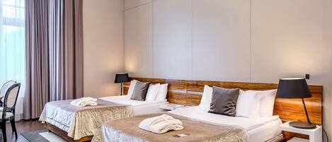 Una habitación de hotel con dos camas, un escritorio, una silla y un ventanal con cortinas.