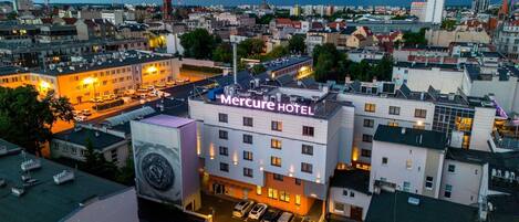 A hotel with a prominent sign, surrounded by urban buildings and a clear sky.