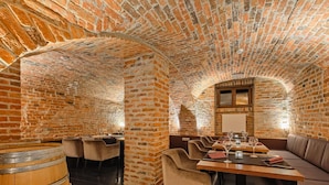 Een restaurant met bakstenen muren en gewelfde plafonds, met tafels en stoelen, een houten vat en een beklede bank.