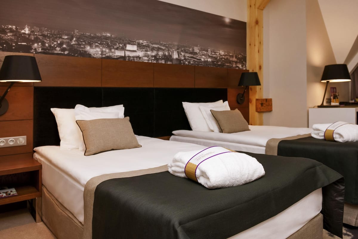 Ein Hotelzimmer mit zwei Betten, Blick auf die Stadt, einem hölzernen Kopfteil, Nachttischlampen und einem Nachttisch mit Lampe.