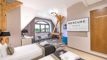 A hotel room with two beds, a desk, a chair, a window with a view, and a sign for Mercure Hotels.