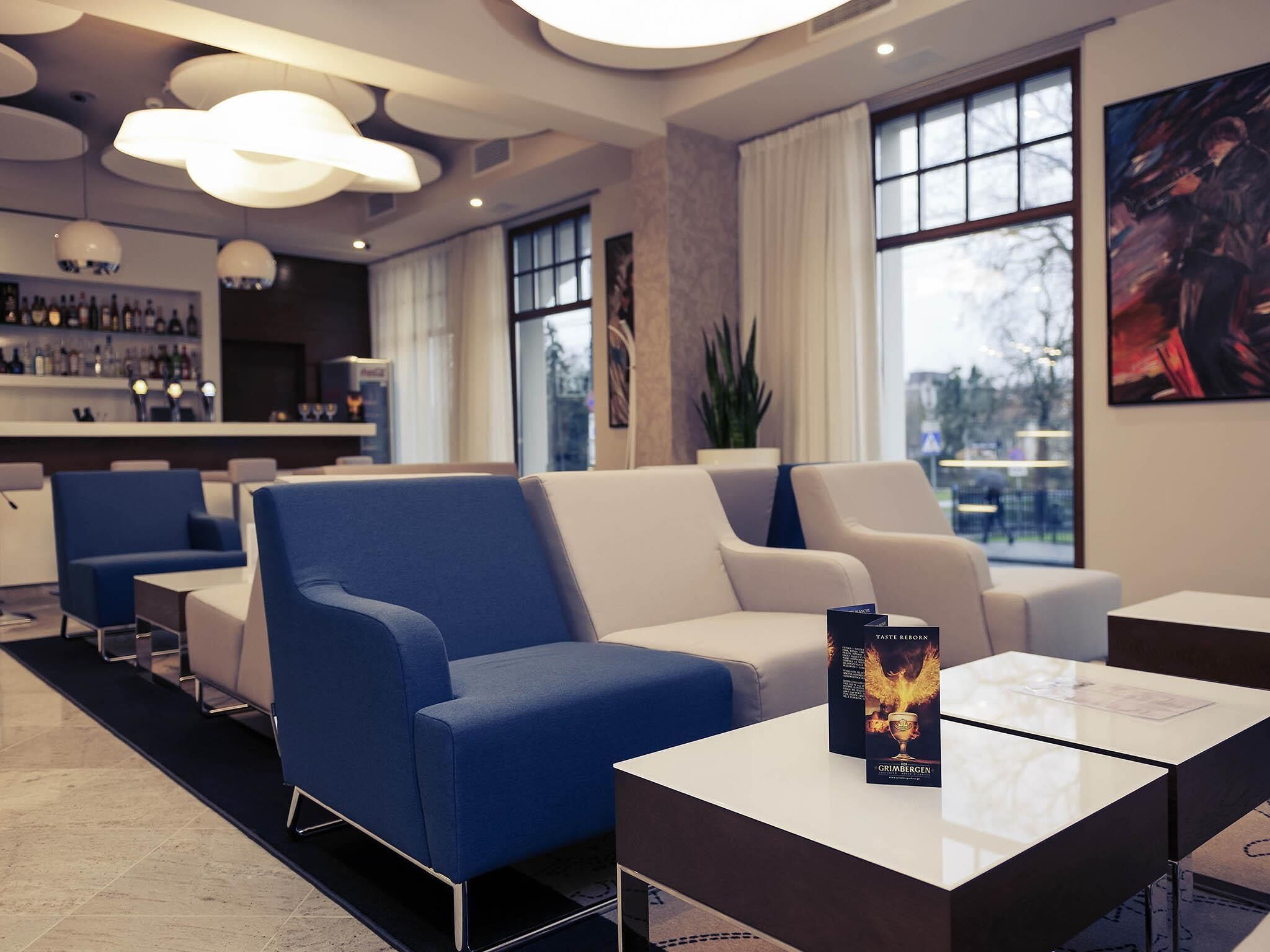 Un moderno vestíbulo de hotel con una zona de bar, espacios de descanso y grandes ventanales.
