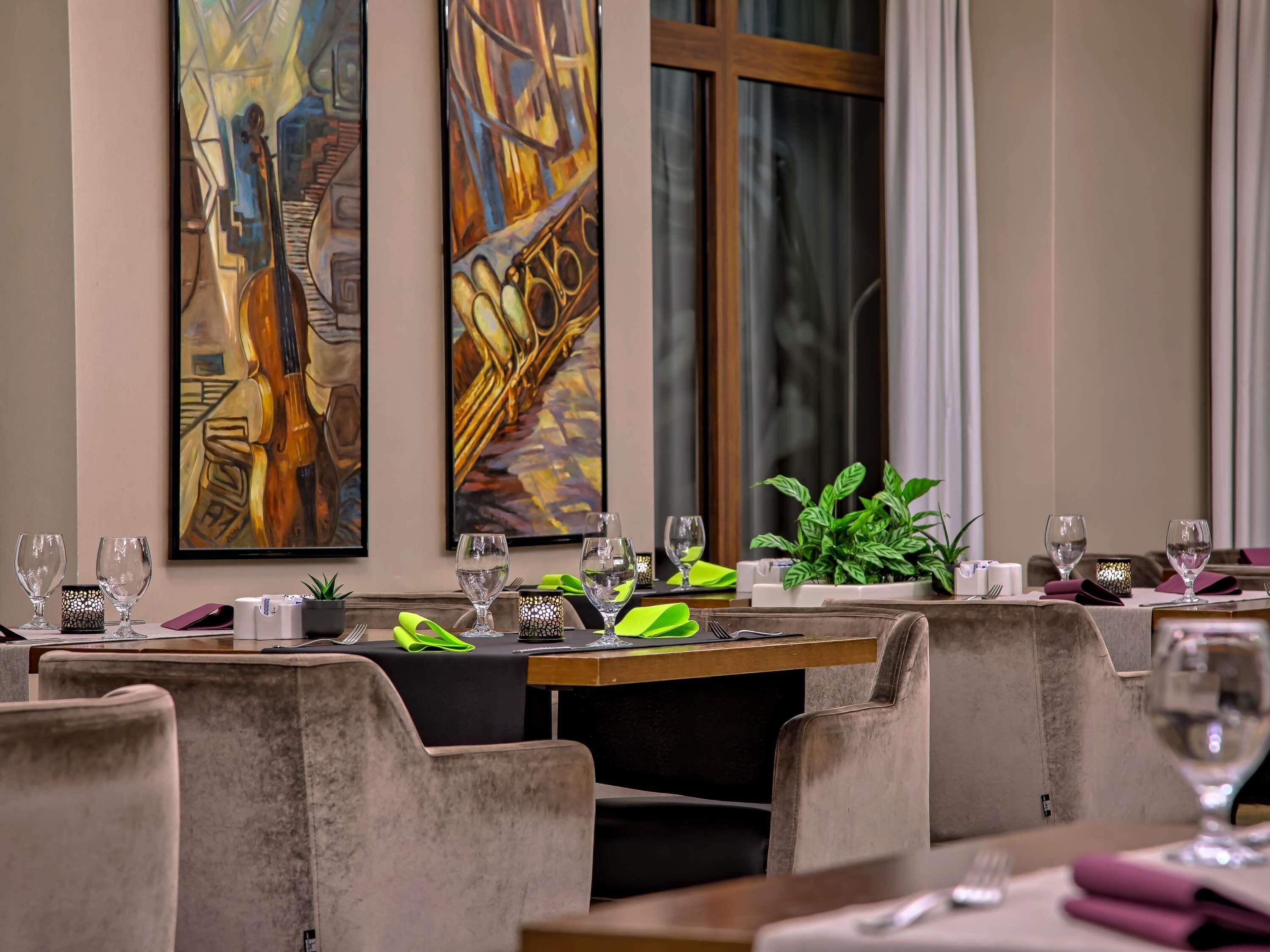 A dining area with tables set for two, featuring modern chairs and a central plant.