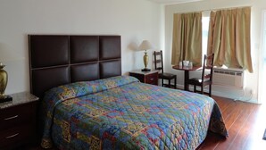 A bedroom with a large bed, a bedside table with a lamp, a small table with chairs, and a window with curtains. - Travel Inn (North Hills)