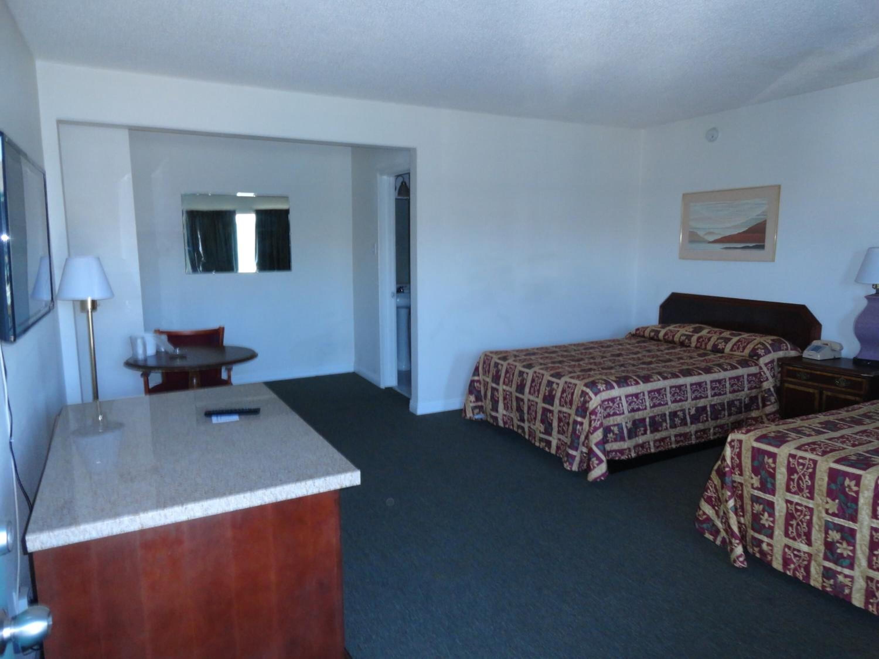 A hotel room with two beds, a desk, a chair, a small table, and a mirror.