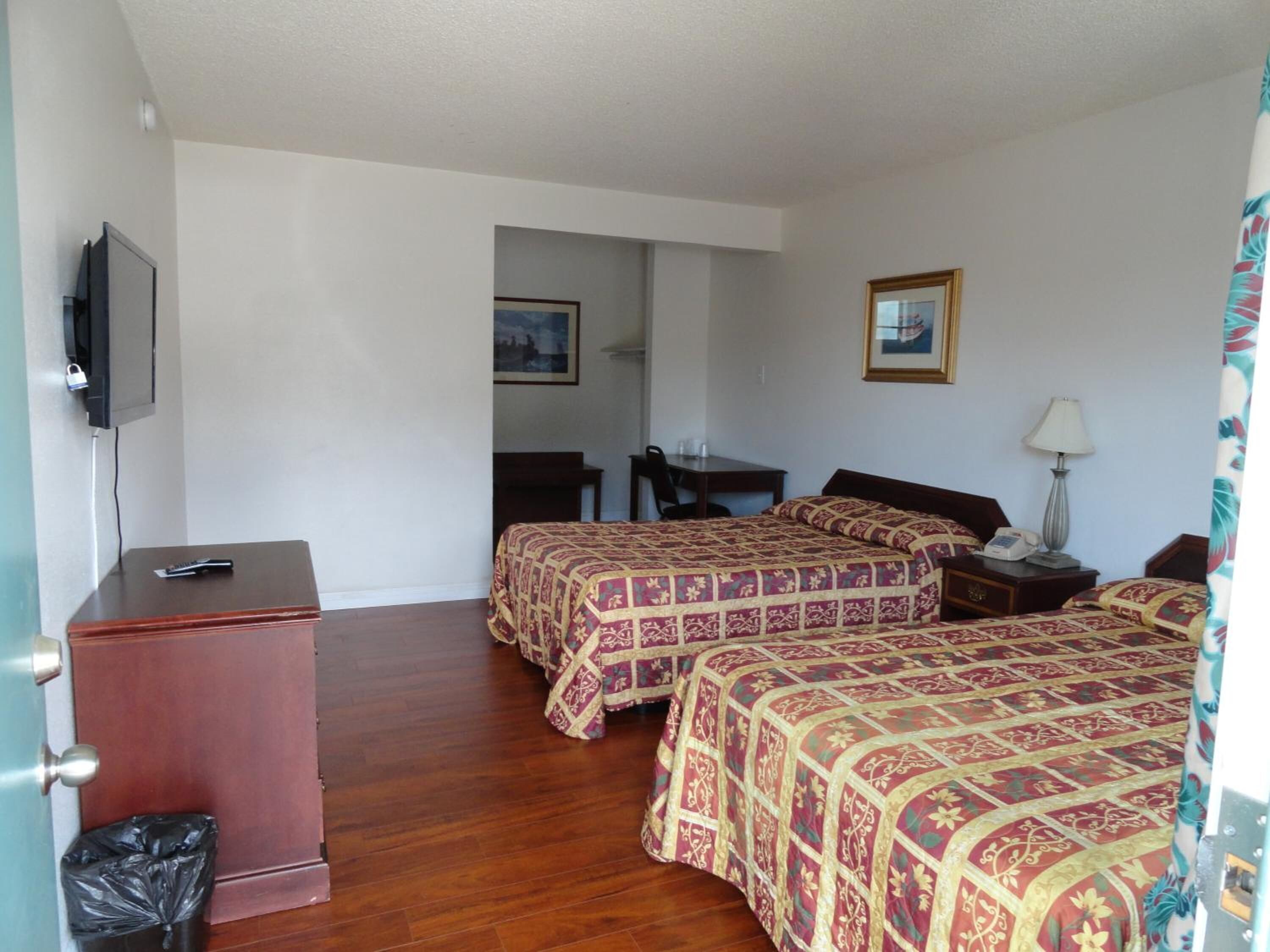 Habitación de hotel con dos camas, un escritorio, una silla, un televisor y un cesto de basura.