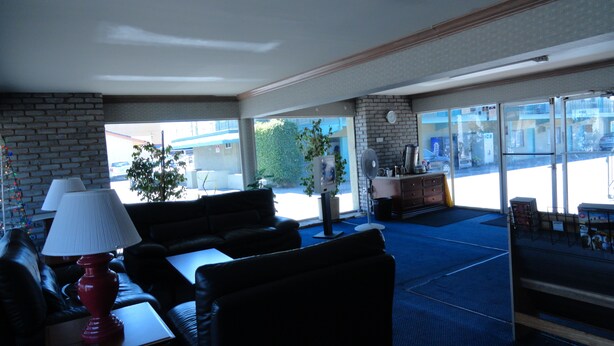 A lobby with a brick wall, a sofa, a table with a lamp, a fan, and a coffee station. - Travel Inn (North Hills)