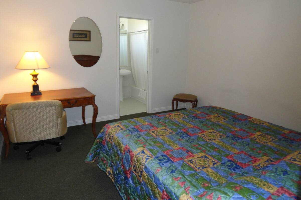 A room with a bed, a desk, a chair, a lamp, and a mirror.