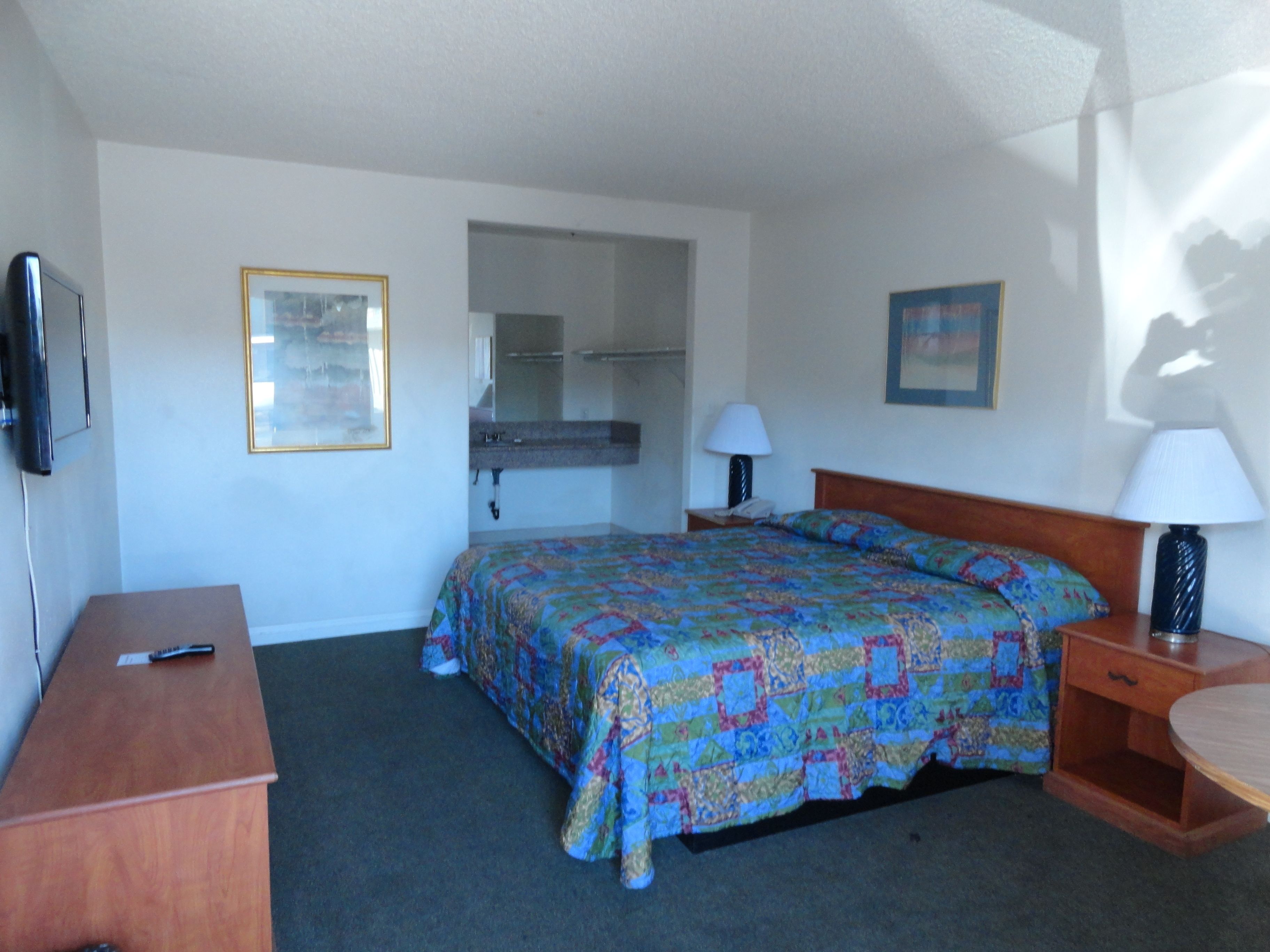 A hotel room with a bed, bedside tables, a desk, a TV, and a bathroom visible through an open door.