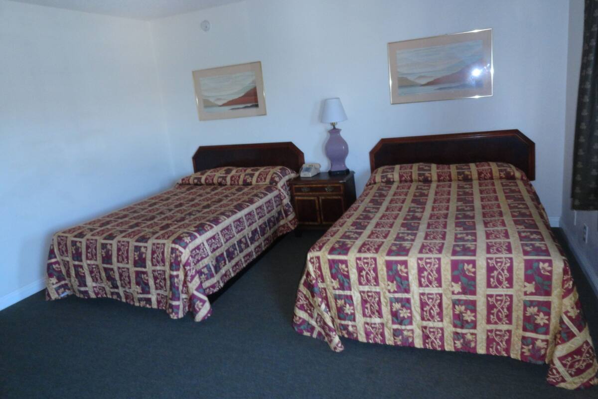 A room with two single beds, a nightstand with a lamp, and two framed pictures on the wall.