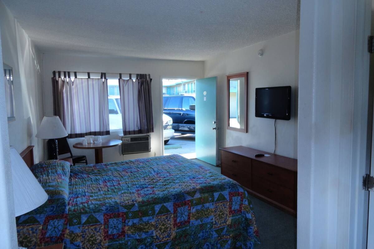 A hotel room with a bed, a desk, a chair, a television, and a view of the outside.