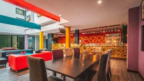 A modern dining area with a long table and multiple chairs, a vibrant red sofa, and a patterned wall in the background.