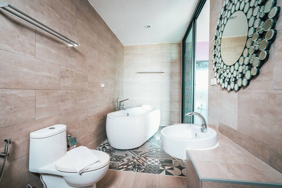 A modern bathroom with a bathtub, toilet, and sink, featuring a patterned floor and a decorative mirror.