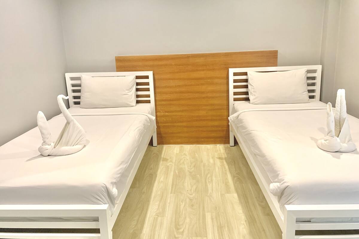 A hotel room with two single beds, each with a wooden headboard and white bedding.