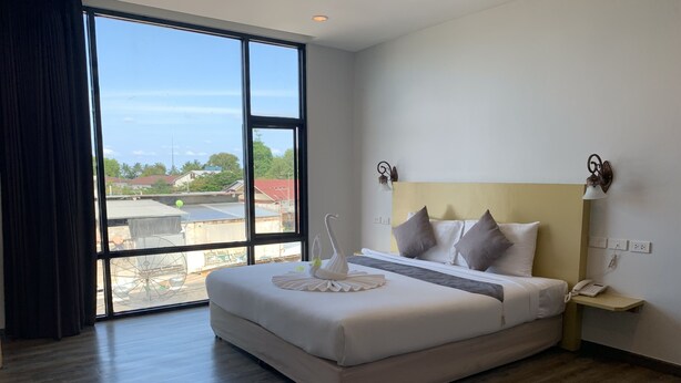 A hotel room with a large bed, a bedside table with a lamp, and a view of the outdoors through a large window.