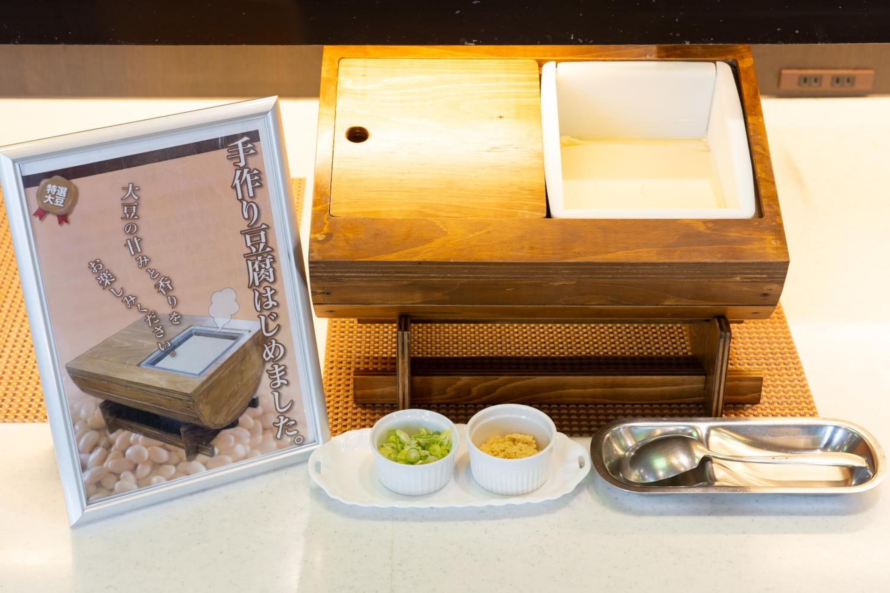A wooden table with a white plate, two bowls of food, and a metal spoon set.