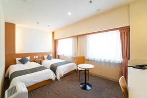 A hotel room with two beds, a small round table, a chair, a desk, and a window with curtains.