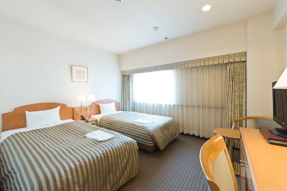 Una habitación de hotel con dos camas, un escritorio, una silla y un televisor.
