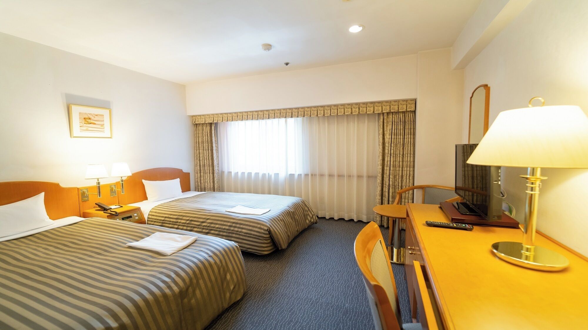 Une chambre d’hôtel avec deux lits, un bureau avec une télévision et une fenêtre avec des rideaux.