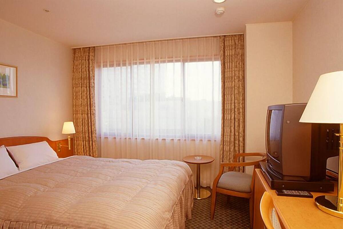 Una habitación de hotel con una cama grande, un televisor, una mesita y una silla.