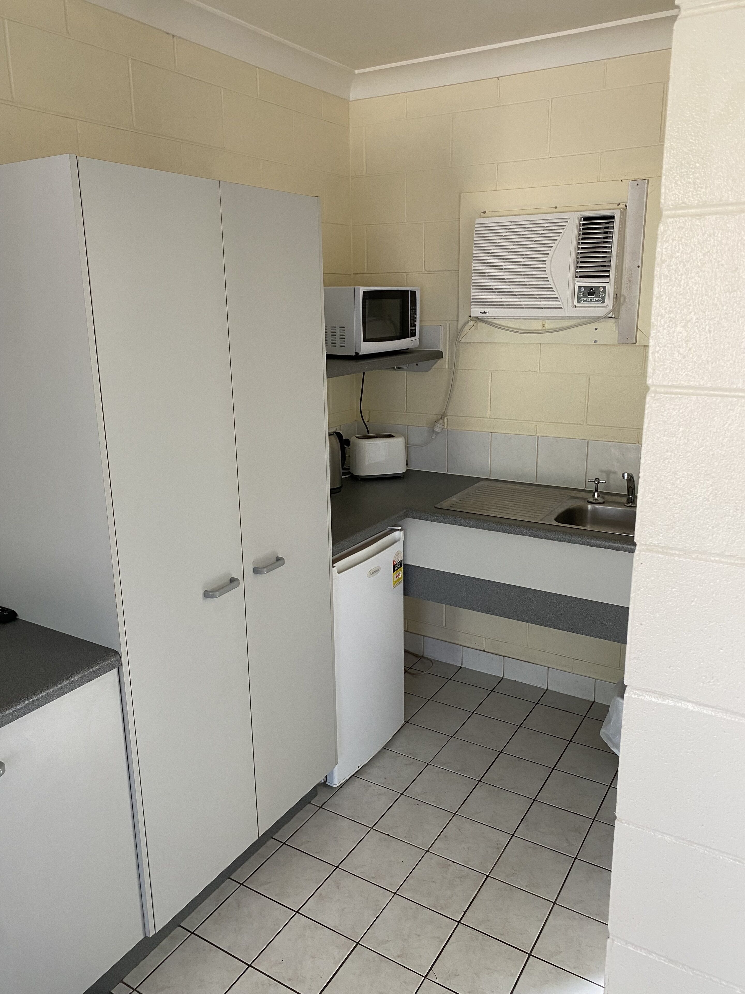 A compact kitchen with a refrigerator, microwave, toaster, and sink.