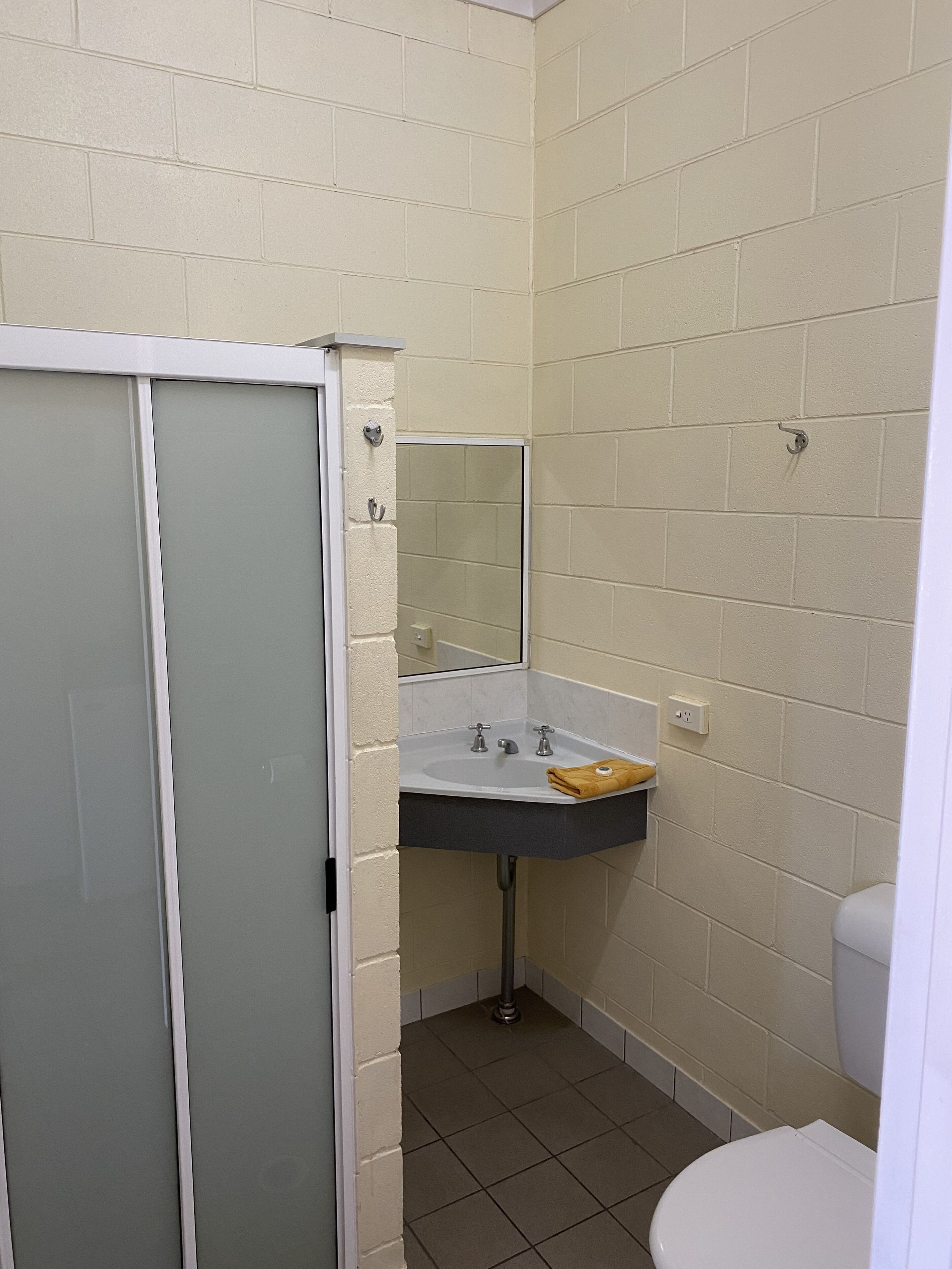 Un baño pequeño con inodoro blanco, lavamanos con espejo y mampara de ducha.