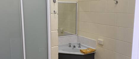 Un baño pequeño con inodoro blanco, lavamanos con espejo y mampara de ducha.