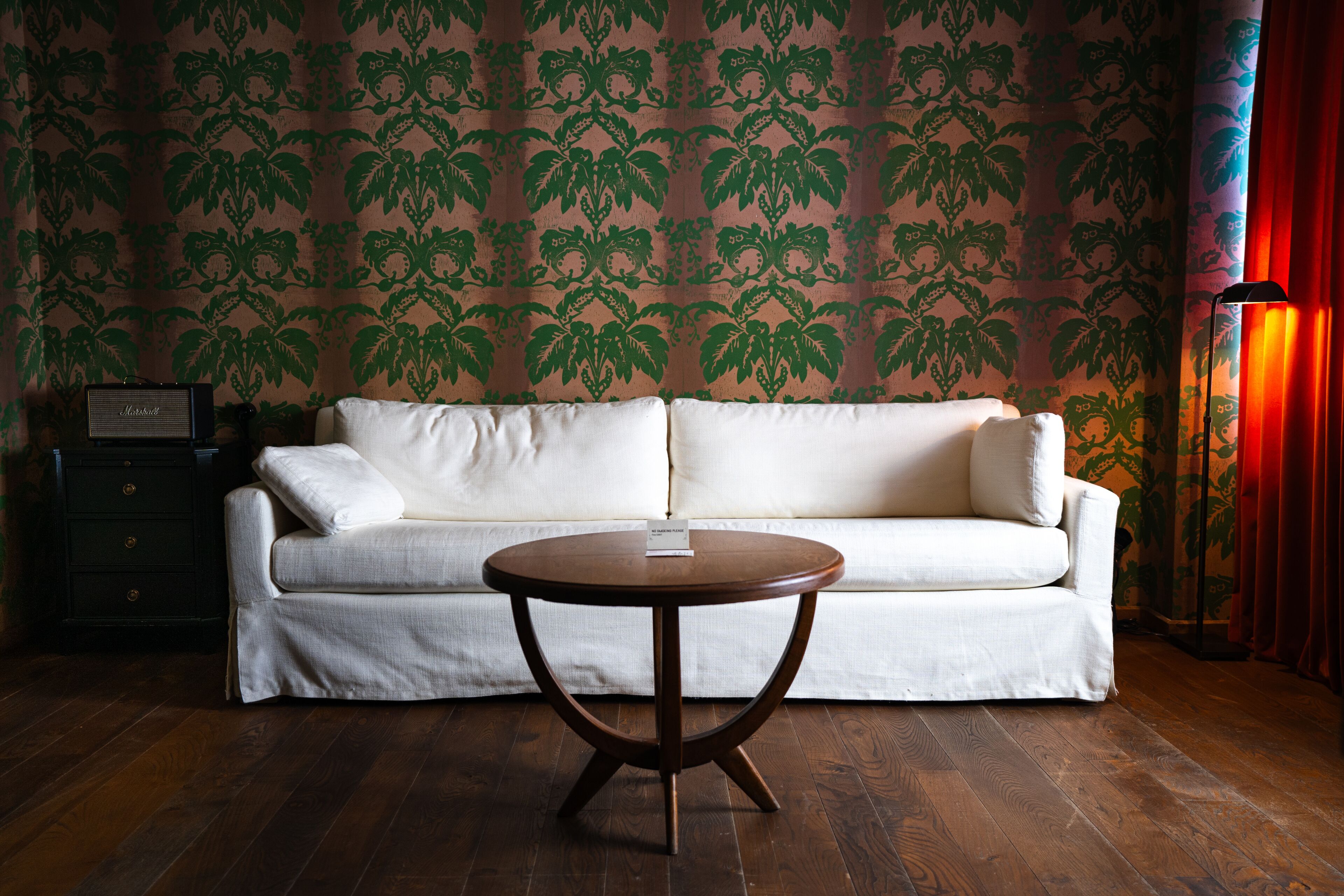 A room with a white sofa, a round wooden table, and a patterned wallpaper.