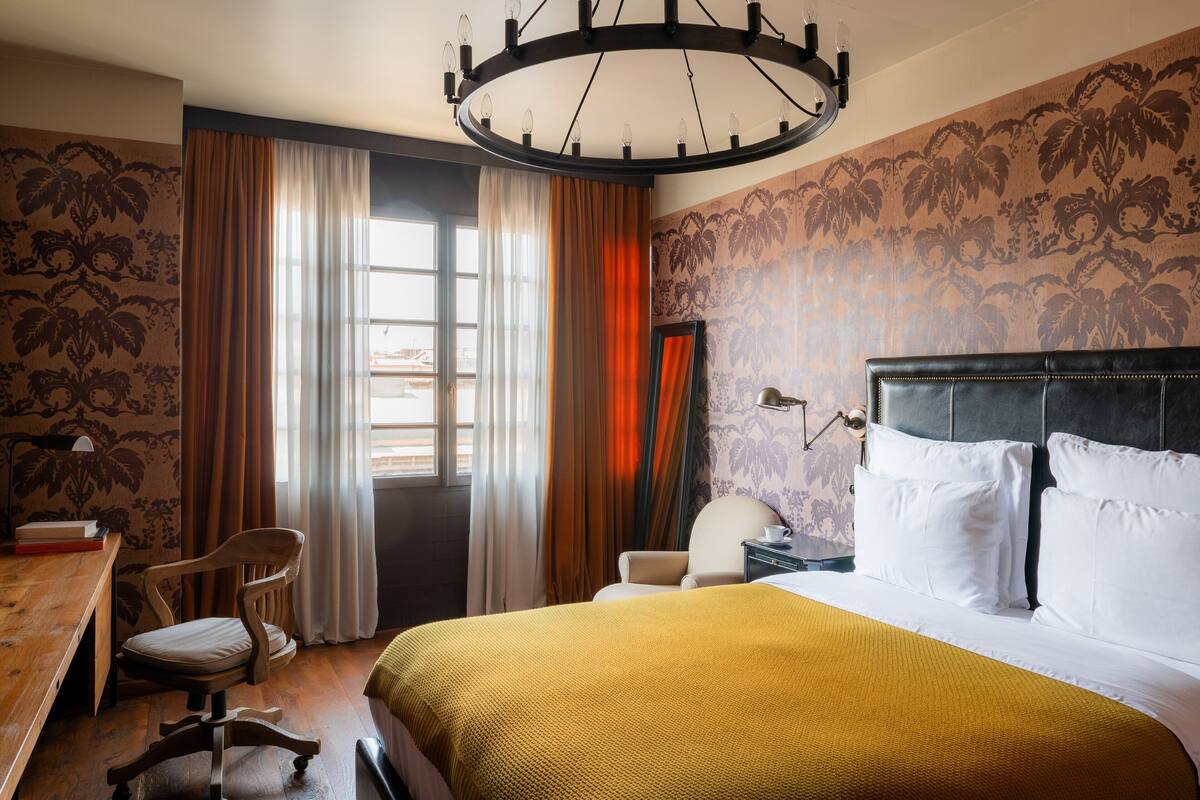 A hotel room with a bed, a desk, a chair, and a large window with curtains.