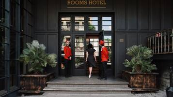 The entrance of Rooms Hotel with a dark facade, large windows, and two potted plants on either side.