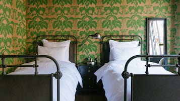 A room with two beds, a nightstand, and a mirror. The walls have a green leafy pattern.