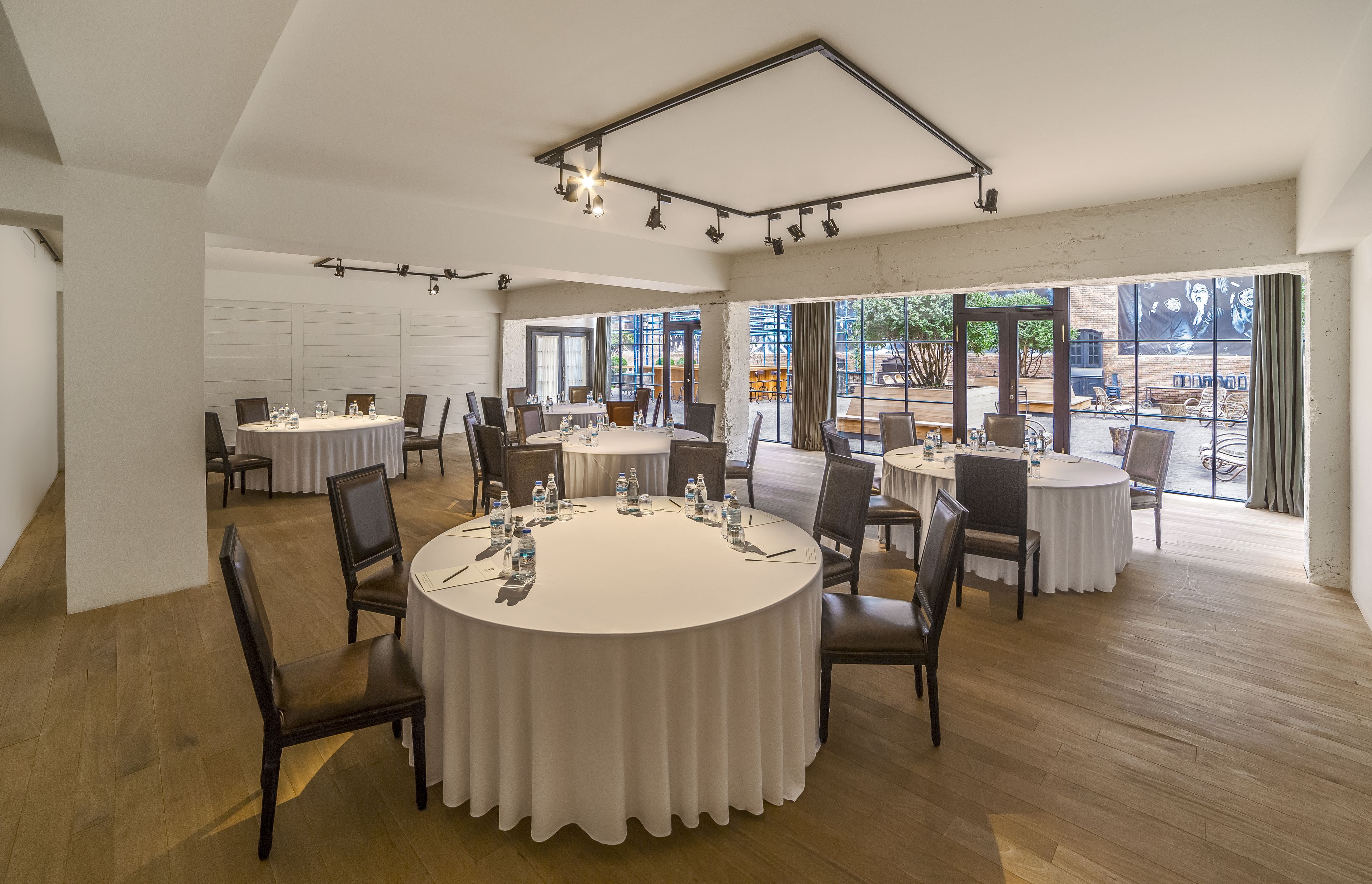 Une salle de conférence équipée de tables rondes, de chaises et d’une grande fenêtre donnant sur l’extérieur.