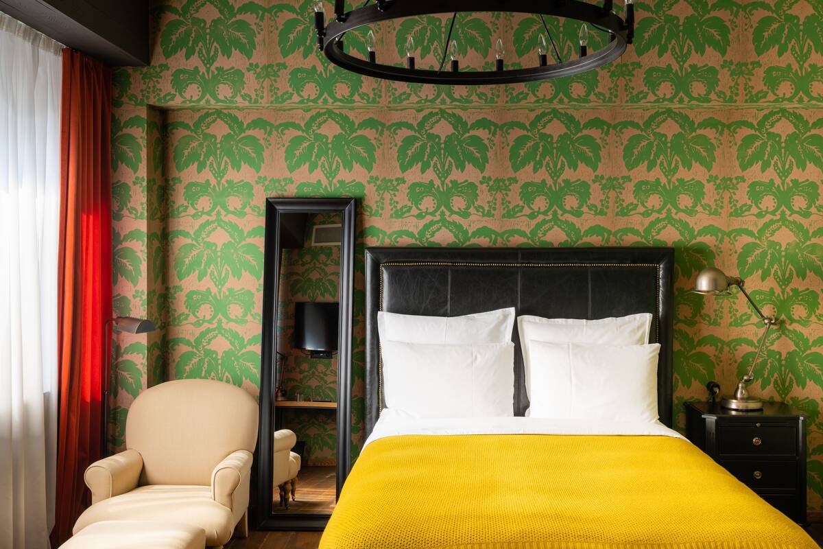 A hotel room with a bed, a chair, a nightstand, and a mirror.