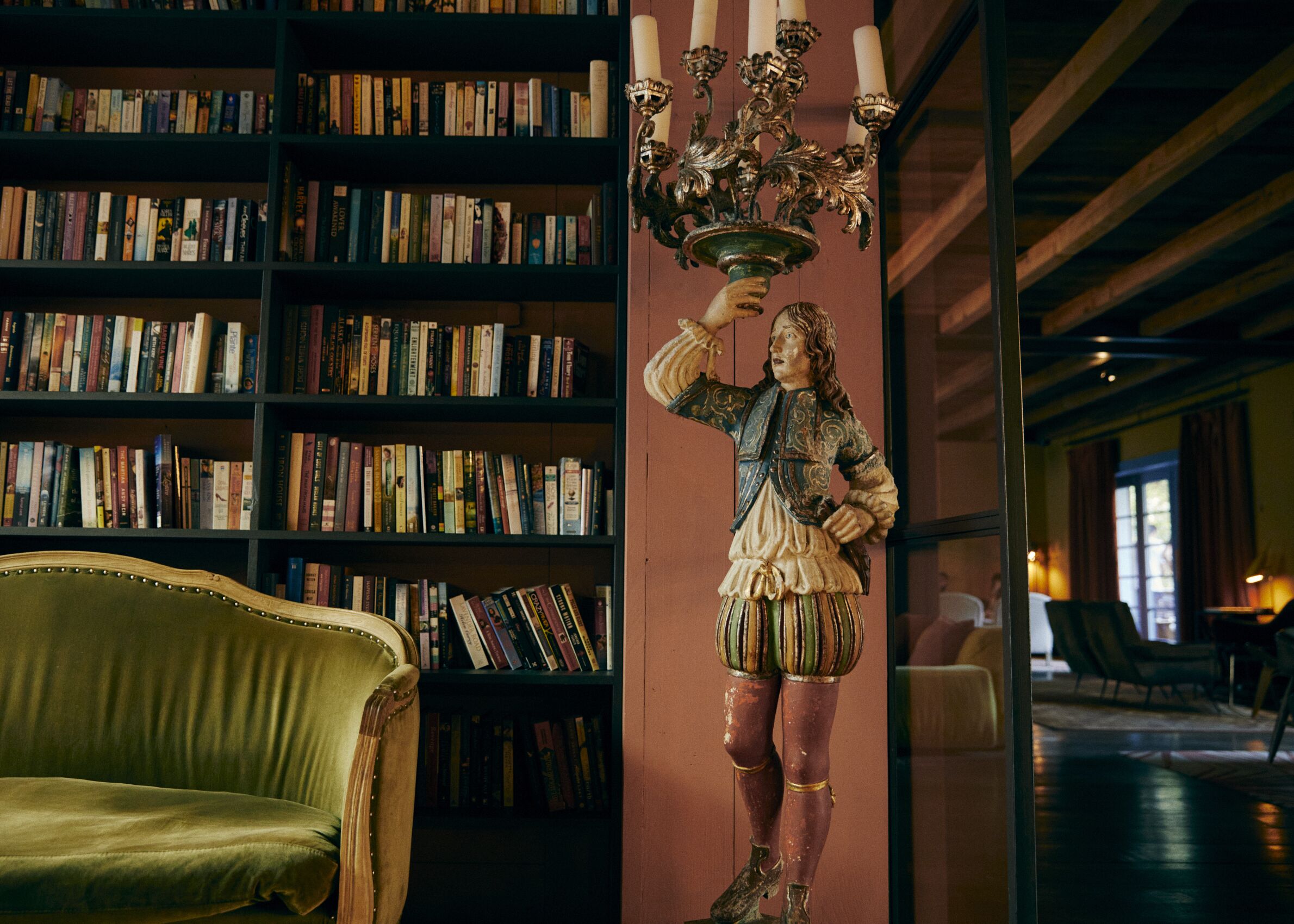 Una biblioteca con estanterías, un sillón verde y una estatua de una figura histórica.