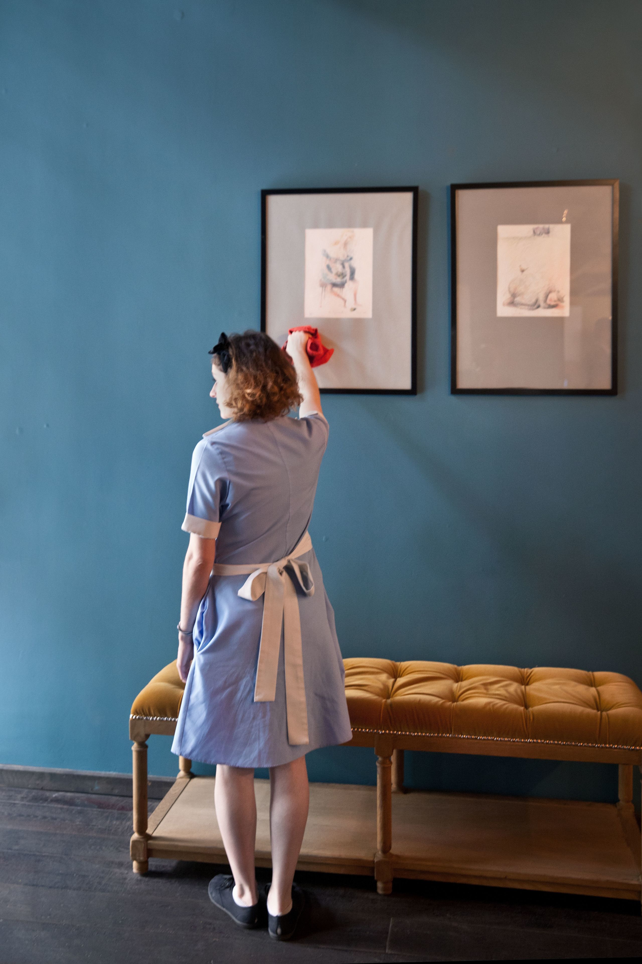 A person standing in front of a blue wall with two framed artworks.
