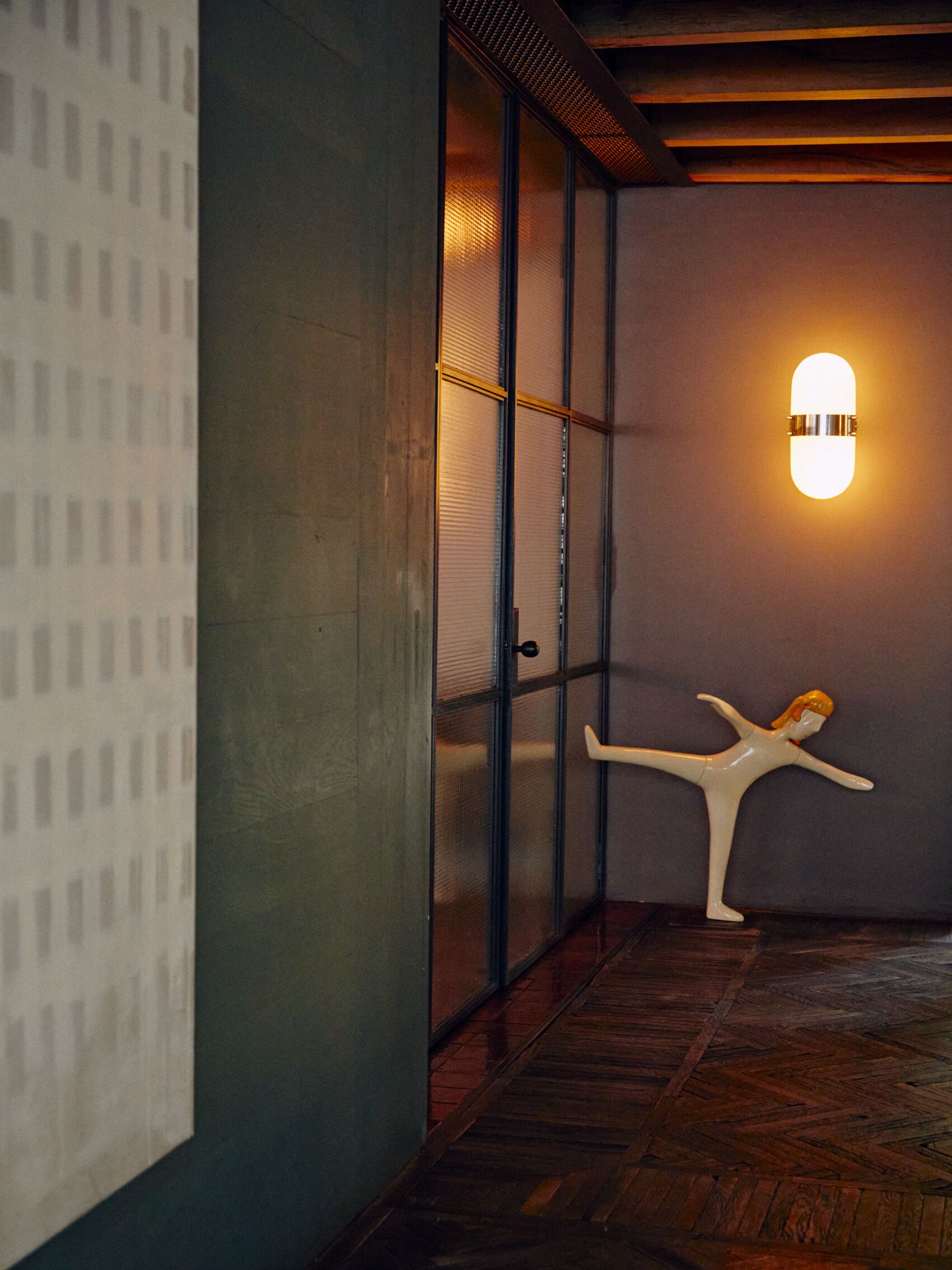 Un pasillo con suelo de madera, una lámpara de pared y una escultura blanca.