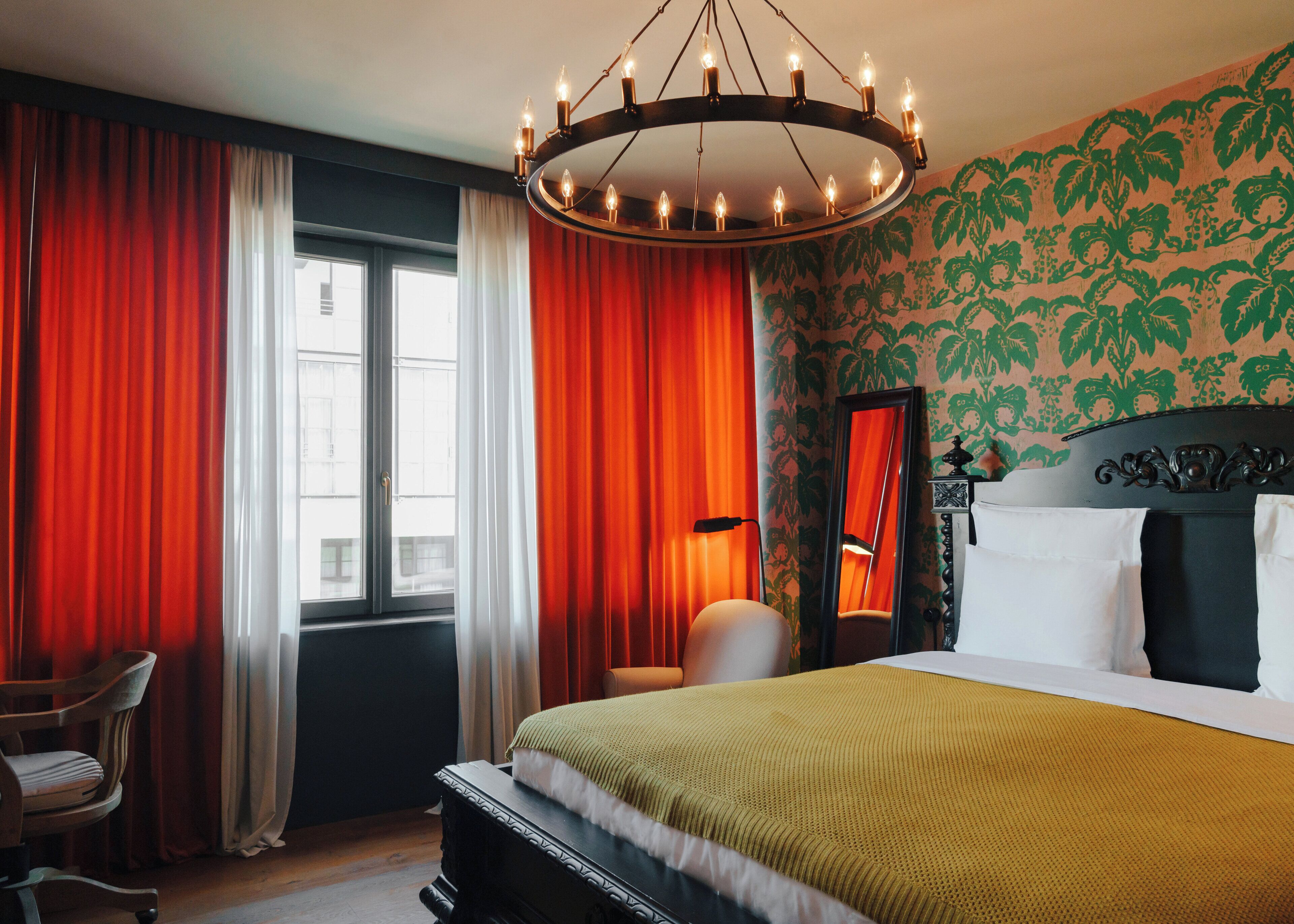 Een hotelkamer met een bed, een stoel, een raam met gordijnen en een kroonluchter.