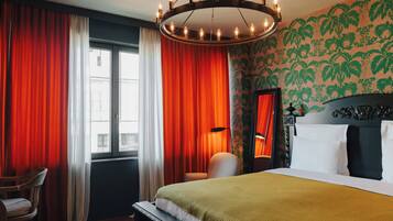Een hotelkamer met een bed, een stoel, een raam met gordijnen en een kroonluchter.