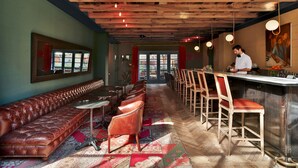 Un espace bar avec un long banc et des tabourets, un plafond en bois et un barman derrière le comptoir.