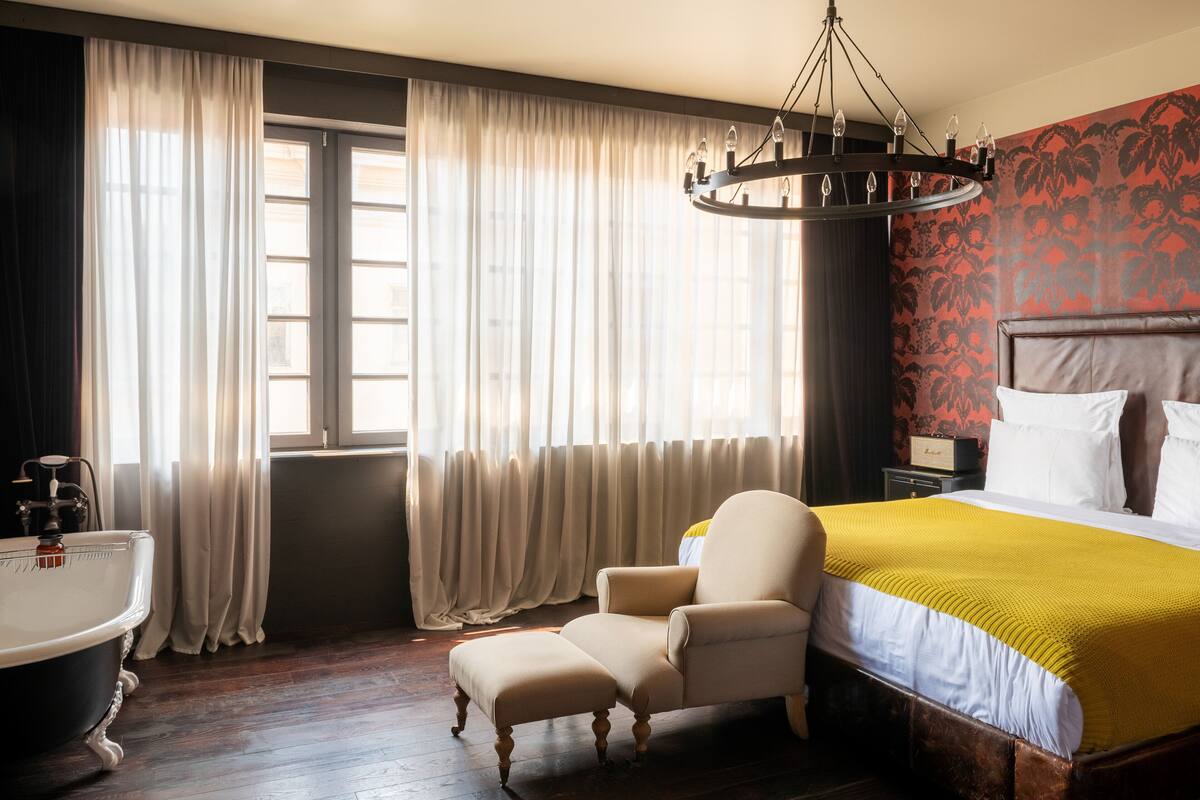 A hotel room with a large bed, a chair, a bathtub, and a chandelier.
