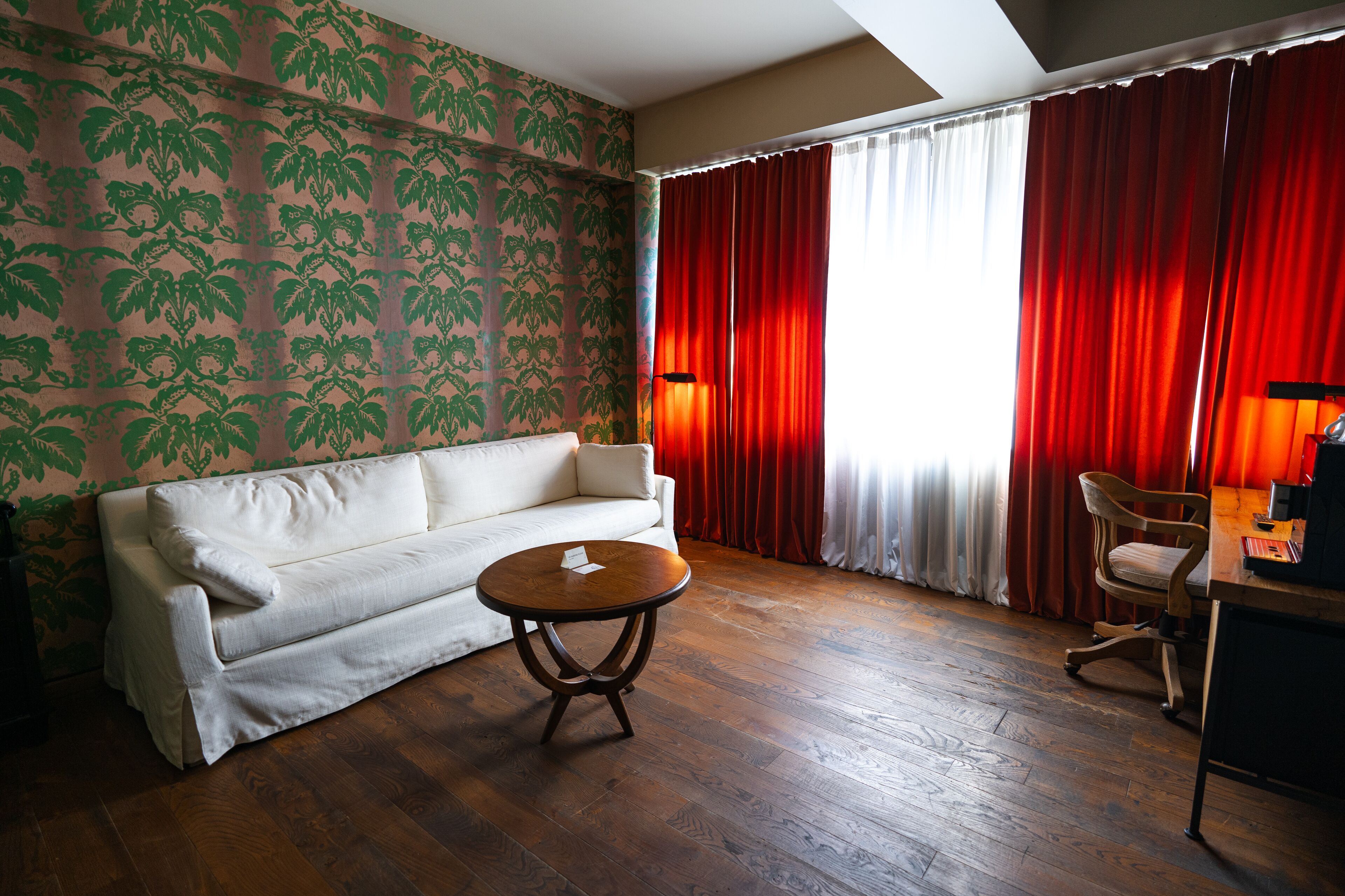 Um quarto com um sofá branco, uma mesa redonda de madeira e uma cadeira de madeira.