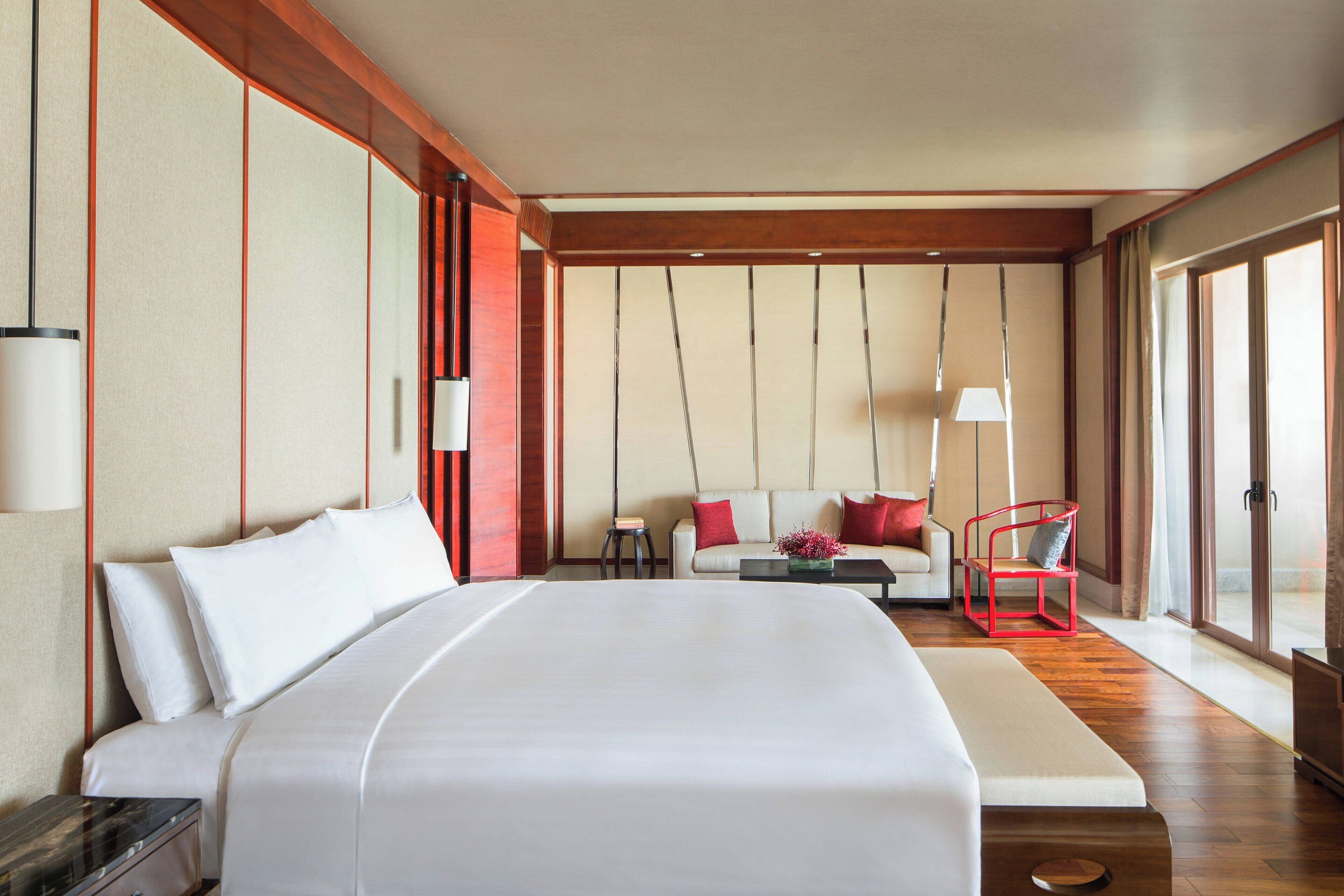 Una habitación de hotel con una cama grande, un sofá, una silla roja, una mesita y una lámpara.